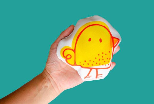 a hand holding a yellow pillow with a bird on it